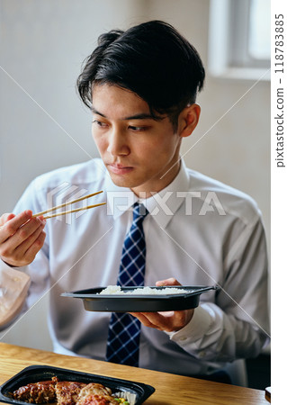 一個20多歲的年輕人，一邊吃便當一邊工作 118783885