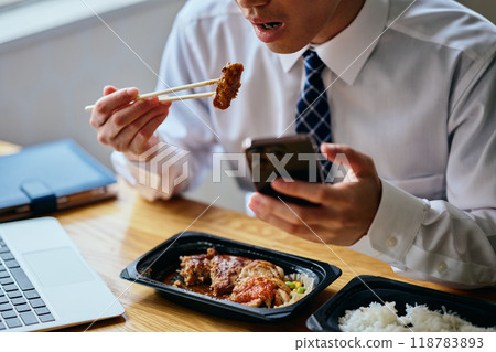 A young man in his twenties operating a smartphone while eating lunch 118783893