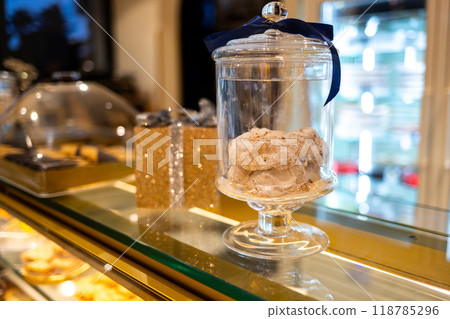 Decorative golden shiny box tied with silver ribbon surrounded by desserts. Christmas or New Year decoration in a cafe. 118785296