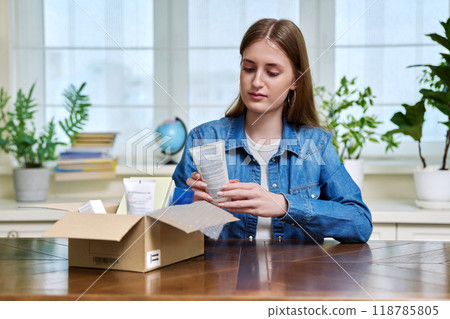 Young female customer sitting at home unpacking cardboard box with online purchases Young female customer sitting at home unpacking cardboard box with online purchases 118785805