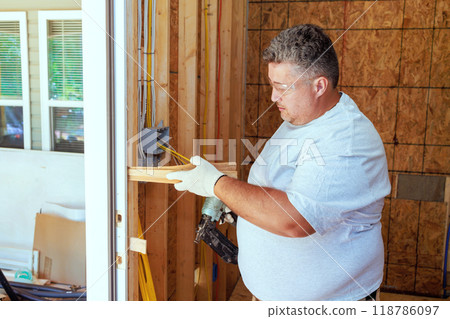 An carpenter uses pneumatic nail gun to install new front door in house An carpenter uses pneumatic nail gun to install new front door in house 118786097