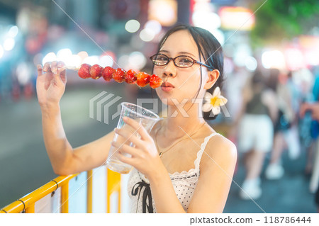 Young adult asian foodie woman eating chinese dessert Tanghulu at china town asia street food Young adult asian foodie woman eating chinese dessert Tanghulu at china town asia street food 118786444