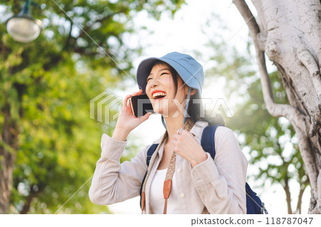 Young adult asian woman traveller wear blue hat and backpack using mobile phone internet for calling on travel. 118787047