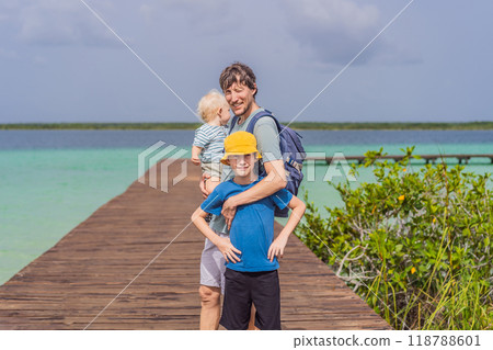 Father with his toddler and teenage sons exploring wooden pier over the turquoise waters of Bacalar Lake, Mexico. Peaceful tropical travel destination concept Father with his toddler and teenage sons exploring wooden pier over the turquoise waters of Bacalar Lake, Mexico. Peaceful tropical travel destination concept 118788601
