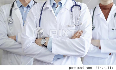 Group of doctors wearing white coats and stethoscopes standing with arms crossed. Medical team at work Group of doctors wearing white coats and stethoscopes standing with arms crossed. Medical team at work 118789114