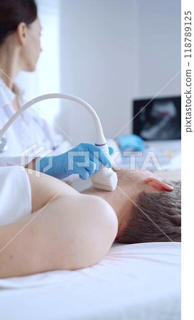 Doctor woman wearing blue medical gloves performing neck ultrasound exam on male patient. Medicine service concept Doctor woman wearing blue medical gloves performing neck ultrasound exam on male patient. Medicine service concept 118789125
