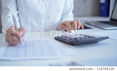 Businesswoman with white blues is using dark calculator and taking notes in her office. Taxes and audit in business 118789126