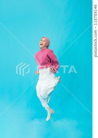 A Joyful Young Woman Enthusiastically Jumping in a Bright and Colorful Studio Setting with Backdrop A Joyful Young Woman Enthusiastically Jumping in a Bright and Colorful Studio Setting with Backdrop 118789146
