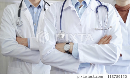 Group of doctors wearing white coats and stethoscopes standing with arms crossed. Medical team at work Group of doctors wearing white coats and stethoscopes standing with arms crossed. Medical team at work 118789150