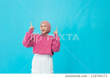 A Cheerful Young Woman Wearing a Pink Sweater and a White Skirt is Posing Against a Bright Blue Background 118789171