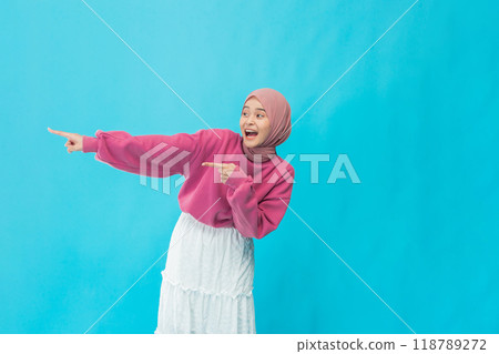 A Joyful Young Woman Pointing with Enthusiasm and Energy Against a Bright and Colorful Blue Background 118789272