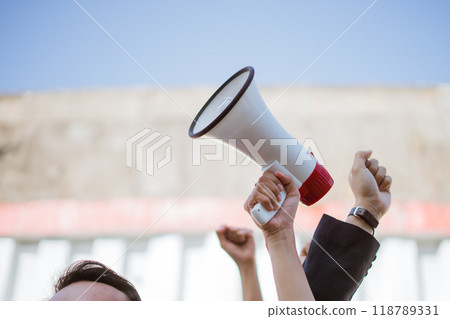 An activist is passionately raising their voice with a megaphone at a protest gathering An activist is passionately raising their voice with a megaphone at a protest gathering 118789331