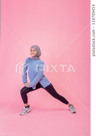 A Young Woman in Stylish Sportswear is Stretching Against a Bright Pink Background, Showing Flexibility A Young Woman in Stylish Sportswear is Stretching Against a Bright Pink Background, Showing Flexibility 118789454