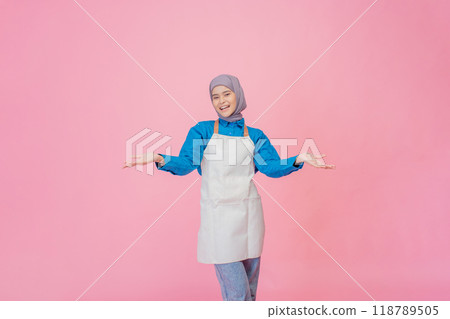 A Cheerful and Young Woman Wearing an Apron Poses Against a Pink Background A Cheerful and Young Woman Wearing an Apron Poses Against a Pink Background 118789505