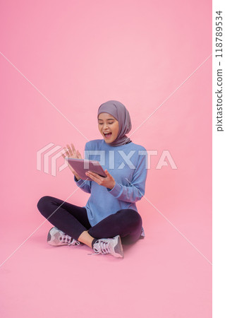 Happy Young Woman using a Tablet on a Bright Pink Background in Casual Outfit Happy Young Woman using a Tablet on a Bright Pink Background in Casual Outfit 118789534