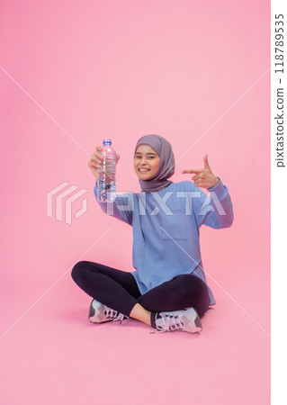 A young woman promoting hydration with a water bottle on a vibrant pink background A young woman promoting hydration with a water bottle on a vibrant pink background 118789535