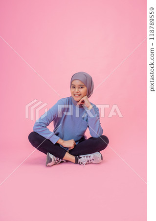 A Young Woman in a Blue Sweater and Stylish Hijab Against a Pink Background 118789559