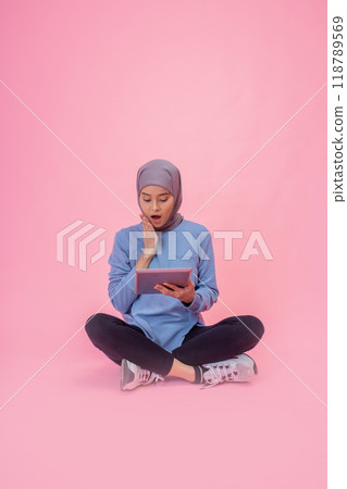 A Young Woman Actively Engaged with Her Tablet Against a Vibrant Pink Background A Young Woman Actively Engaged with Her Tablet Against a Vibrant Pink Background 118789569