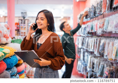 Female entrepreneur using a cell phone while holding a clipboard 118789751