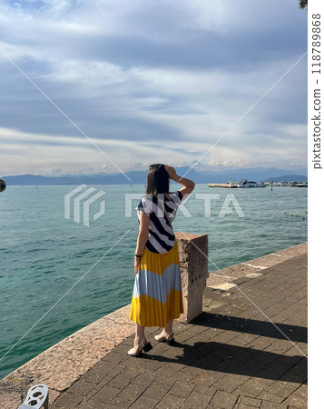 Woman in long dress enjoying stunning view over the Garda lake, seen from Peschiera del Garda 118789868