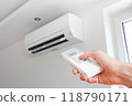 Air conditioner temperature adjustment with remote controller in room at home. Hand holding remote controller of air conditioner inside the white room and set at cool temperature 118790171