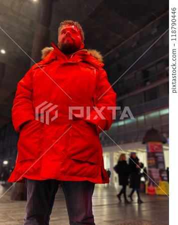 Man walking in a bustling nighttime city street, wearing a bright orange parka. Red neon light. Serene contemplation against the backdrop of lively city lights at night. Urban life concept Man walking in a bustling nighttime city street, wearing a bright orange parka. Red neon light. Serene contemplation against the backdrop of lively city lights at night. Urban life concept 118790446