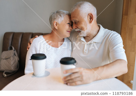 Charming senior couple with gray hair spending quality time together at cafe, foreheads touching as they savor moment of connection over their coffee. Concept of active aging and happy golden years. Charming senior couple with gray hair spending quality time together at cafe, foreheads touching as they savor moment of connection over their coffee. Concept of active aging and happy golden years. 118793186