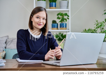 Portrait of young woman at her workplace at desk with laptop, looking at camera Portrait of young woman at her workplace at desk with laptop, looking at camera 118793259