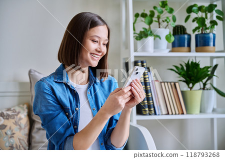 Young woman using smartphone sitting on couch at home 118793268
