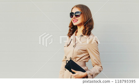 Fashion pretty smiling woman model wearing a coat and black handbag clutch over grey background 118793395