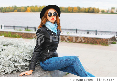 Fashion young woman posing in black rock jacket, hat at city park 118793437