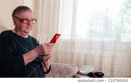 Elderly grandmother holds a smartphone in her hands, using it to connect with loved ones through social media and stay engaged with family Elderly grandmother holds a smartphone in her hands, using it to connect with loved ones through social media and stay engaged with family 118798268