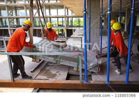 Workers at a building under construction take slabs from a crane Workers at a building under construction take slabs from a crane 118803366