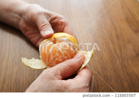 Senior woman's hands peeling mandarin oranges at a table 118803507