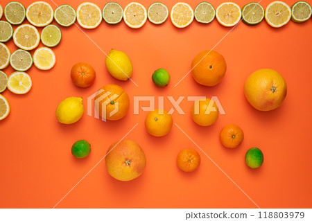 Freshly cut slices of lemons and limes on the upper border and other whole citrus fruits on an orange background. 118803979