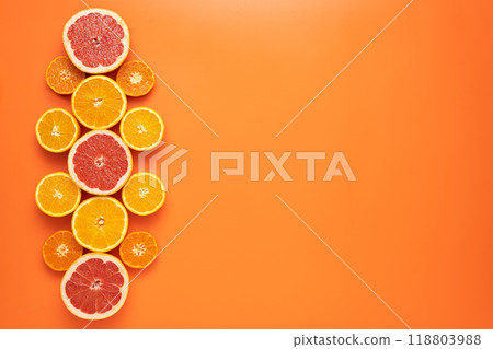 Fresh sliced and halved citrus fruits as a pattern in the left third of the image on an orange background. 118803988