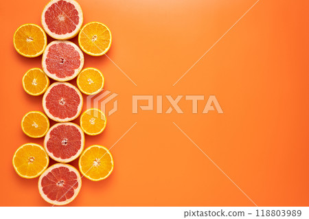 Fresh sliced and halved citrus fruits as a pattern in the left third of the image on an orange background. 118803989