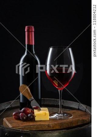 A glass of red wine with a bottle of cheese and grapes on an old wine barrel A glass of red wine with a bottle of cheese and grapes on an old wine barrel 118804212