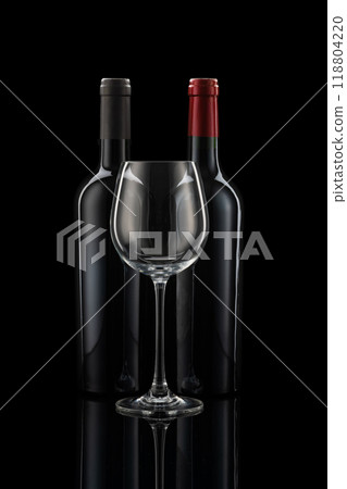 Two wine bottles next to each other, a wine glass in front of a black background 118804220