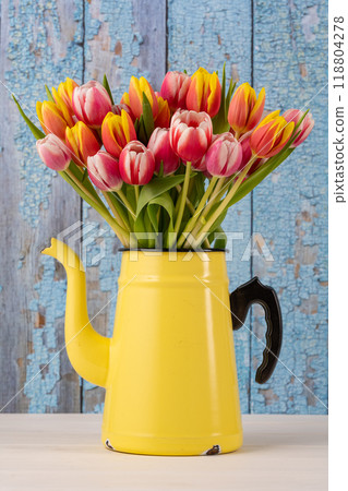 Fresh colorful bouquet of tulips in yellow enamel coffee pot in front of blue old wooden wall 118804278