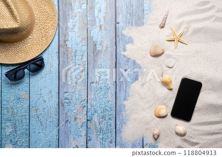 Summer, beach and vacation concept with free text space. Top view. Flat layout with a man straw hat, sun glasses, smartphone, various sea shells and fine beach sand on an old blue wooden boards Summer, beach and vacation concept with free text space. Top view. Flat layout with a man straw hat, sun glasses, smartphone, various sea shells and fine beach sand on an old blue wooden boards 118804913