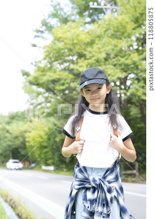 A girl in elementary school walking through the woods on her way to school in the countryside, carrying a backpack A girl in elementary school walking through the woods on her way to school in the countryside, carrying a backpack 118805875