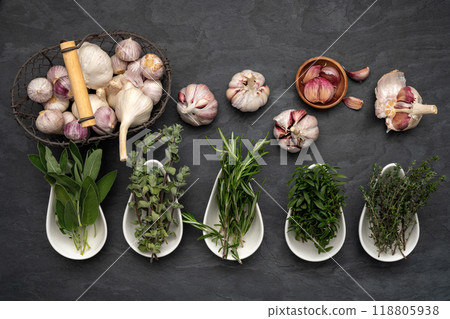 Herbs in porcelain bowls, fresh garlic bulbs in a metal basket 118805938