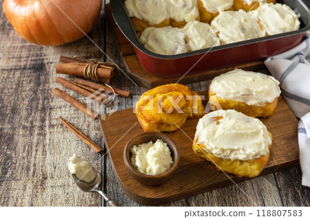 Freshly baked pumpkin cinnamon rolls or cinnabon with cream cheese on a rustic wooden table. Homemade seasonal autumn homemade pastry. 118807583