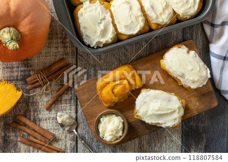 Freshly baked pumpkin cinnamon rolls or cinnabon with cream cheese on a rustic wooden table. Homemade seasonal autumn homemade pastry. 118807584