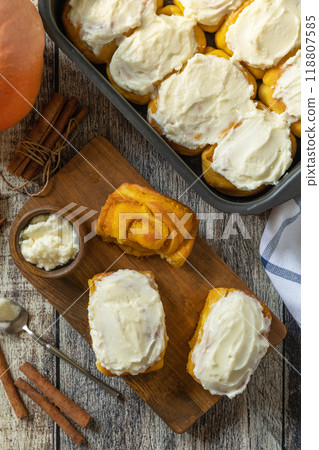 Freshly baked pumpkin cinnamon rolls or cinnabon with cream cheese on a rustic wooden table. Homemade seasonal autumn homemade pastry. 118807585