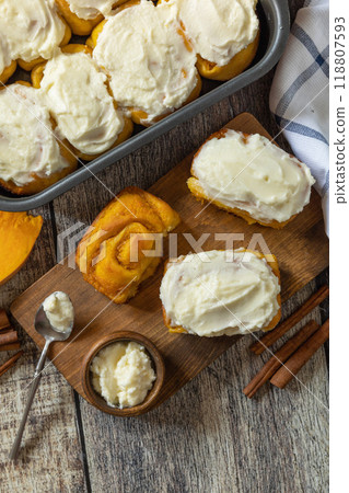 Freshly baked pumpkin cinnamon rolls or cinnabon with cream cheese on a rustic wooden table. Homemade seasonal autumn homemade pastry. Freshly baked pumpkin cinnamon rolls or cinnabon with cream cheese on a rustic wooden table. Homemade seasonal autumn homemade pastry. 118807593