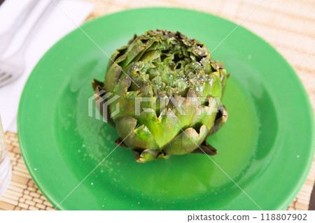 Cooked whole artichoke on a green plate Cooked whole artichoke on a green plate 118807902
