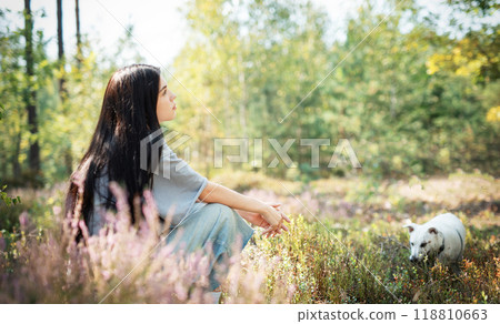 A young woman enjoys a quiet moment in a sunlit field with her white dog  118810663