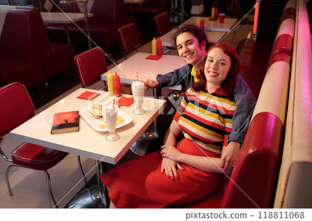 Smiling Couple Sitting at Retro Diner Booth Enjoying Milkshakes 118811068